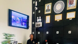 Una recepción con mostrador negro, una planta en maceta y una televisión instalada en la pared.