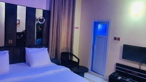 Una habitación de hotel con una cama, un escritorio, una silla, un televisor y una puerta.