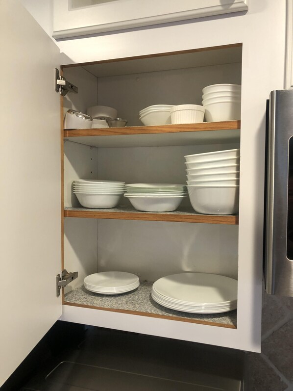 Un mueble de cocina con varios estantes que contienen platos y cuencos blancos.