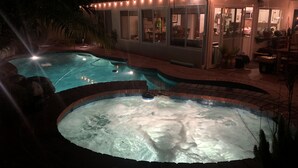 Una piscina con jacuzzi, rodeada por una solería de ladrillo y palmeras.