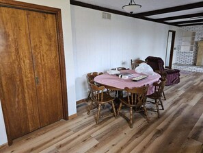 Un coin repas avec une table et des chaises en bois, une porte en bois et un mur en briques en arrière-plan.