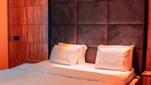 A neatly made bed with white linens and pillows, a wooden headboard, and a small wooden nightstand beside it. - Old English Torf Apartment (Owerri)