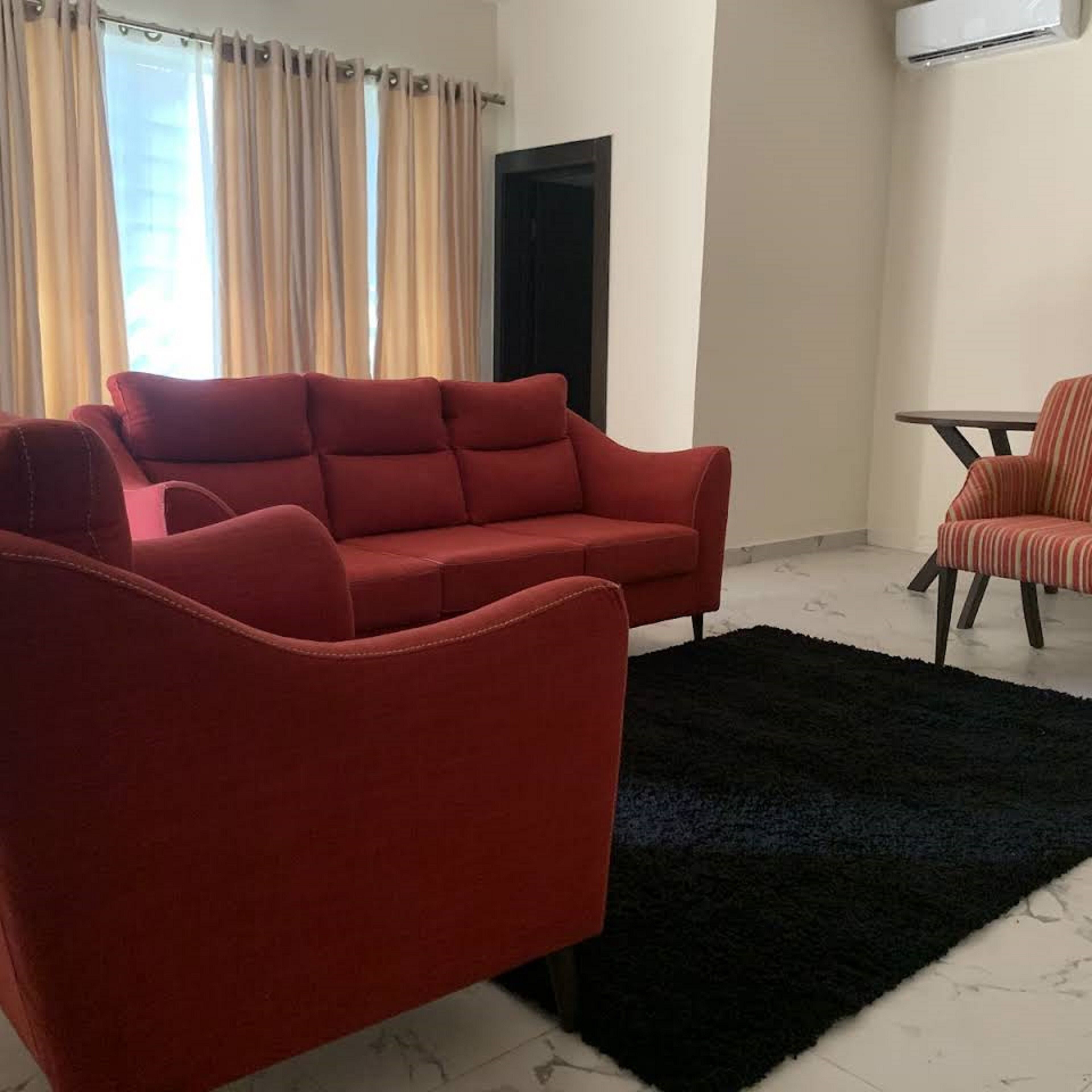 Una sala de estar con un sofá rojo, una alfombra negra y una silla a rayas.