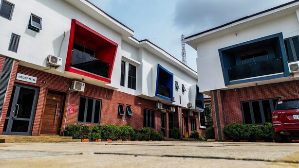 A modern building with a reception area, a red and blue facade, and a parked car. - Old English Torf Apartment (Owerri)