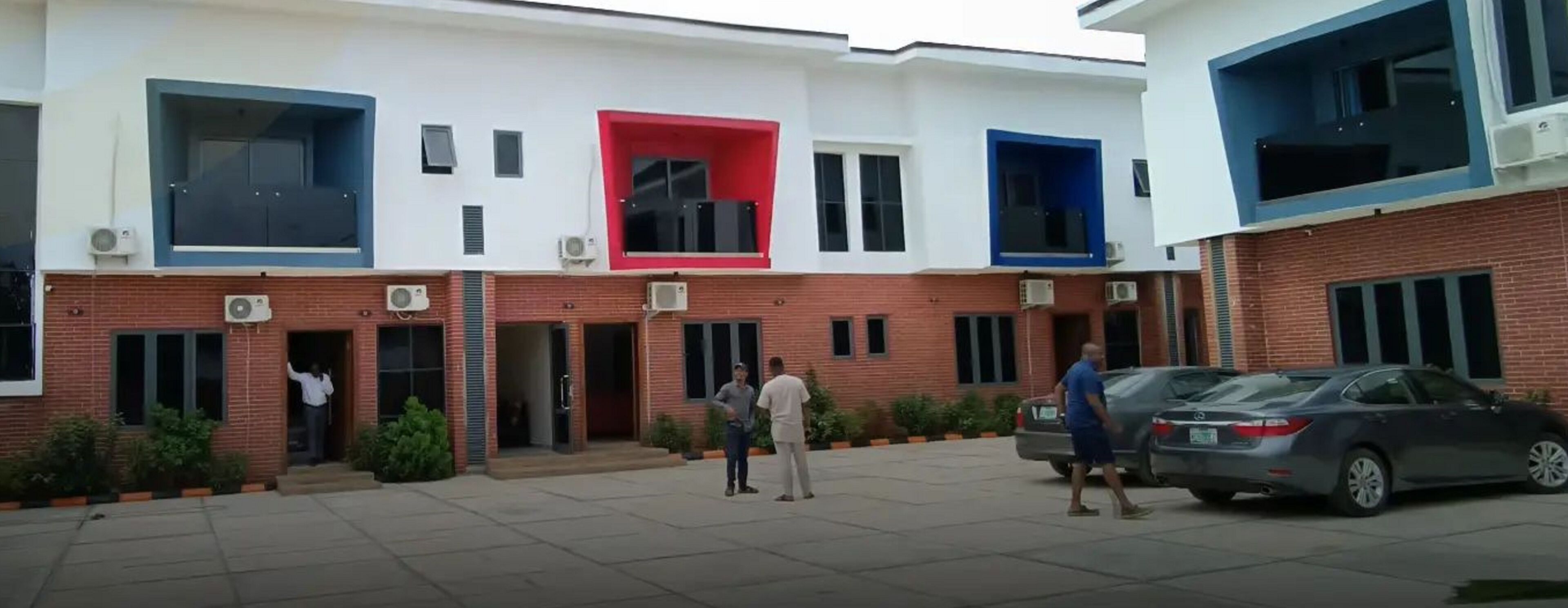 A modern building with a red, blue, and white facade, featuring multiple windows and air conditioning units.