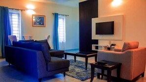 A modern living room with a sofa, armchair, coffee table, and a flat-screen TV mounted on the wall. - Old English Torf Apartment (Owerri)
