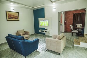 A living room with a TV, two sofas, a coffee table, and a brick wall. - Old English Torf Apartment (Owerri)