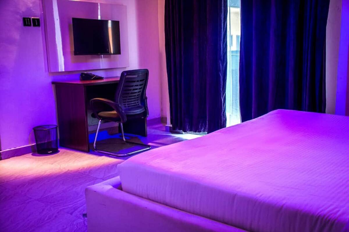 A hotel room with a bed, a desk with a chair, a television, and a window with curtains.