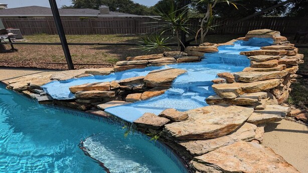 A swimming pool with a rocky waterfall feature and a curved edge. - Large 4bd 2bth pool home with hot tub, waterfall feature and private back yard! (Palm Bay)