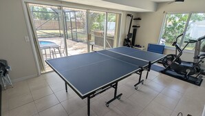 A room with a ping pong table, exercise equipment, and a sliding glass door to the outdoors. - Large 4bd 2bth pool home with hot tub, waterfall feature and private back yard! (Palm Bay)