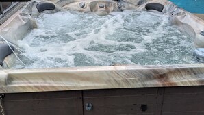 A hot tub with a wooden exterior, a glass enclosure, and a pool in the background. - Large 4bd 2bth pool home with hot tub, waterfall feature and private back yard! (Palm Bay)
