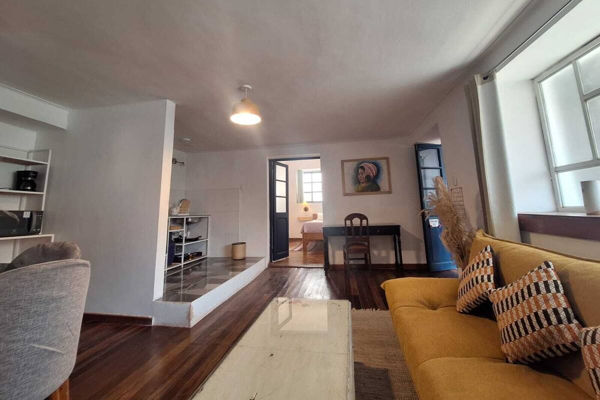A living room with a sofa, a coffee machine, and a dining area in the background.
