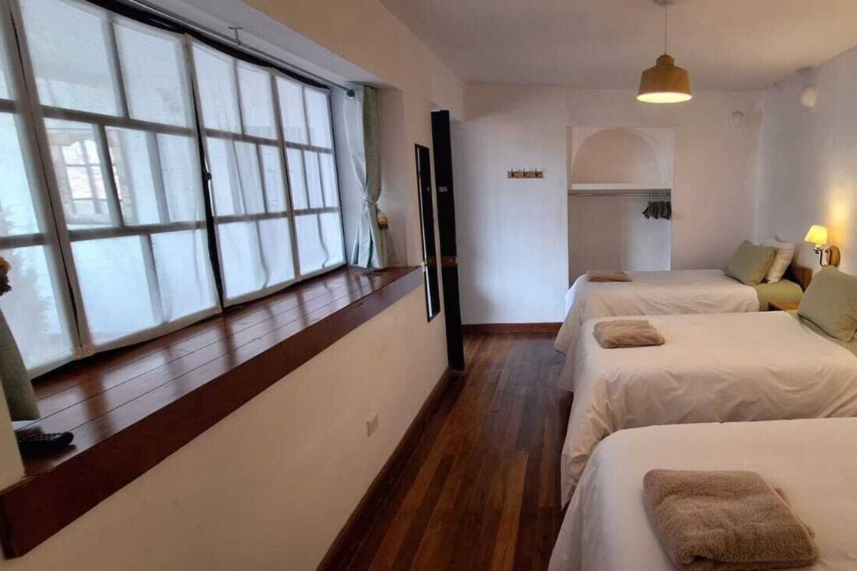 A hotel room with two beds, a window with curtains, a wooden floor, and a hanging light fixture.