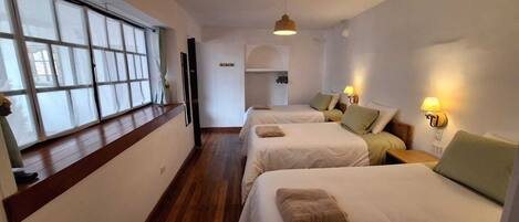 A hotel room with two beds, a window with curtains, a wooden floor, and a hanging light fixture.
