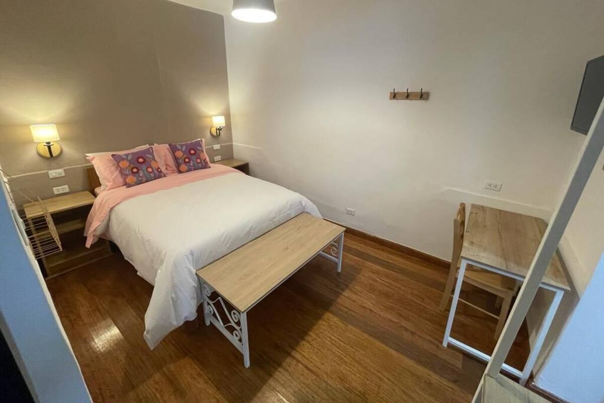 A bedroom with a bed, bedside tables, a bench, and a hanging light fixture.