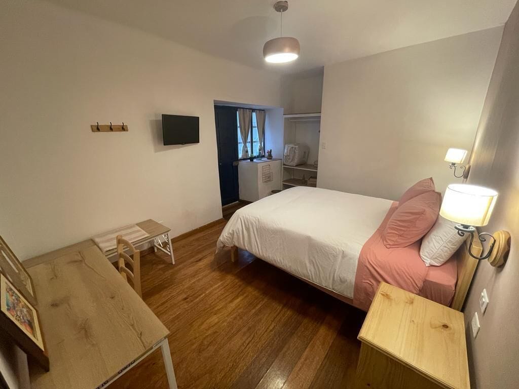 A bedroom with a bed, bedside table, wooden floor, wardrobe, and a TV on the wall.