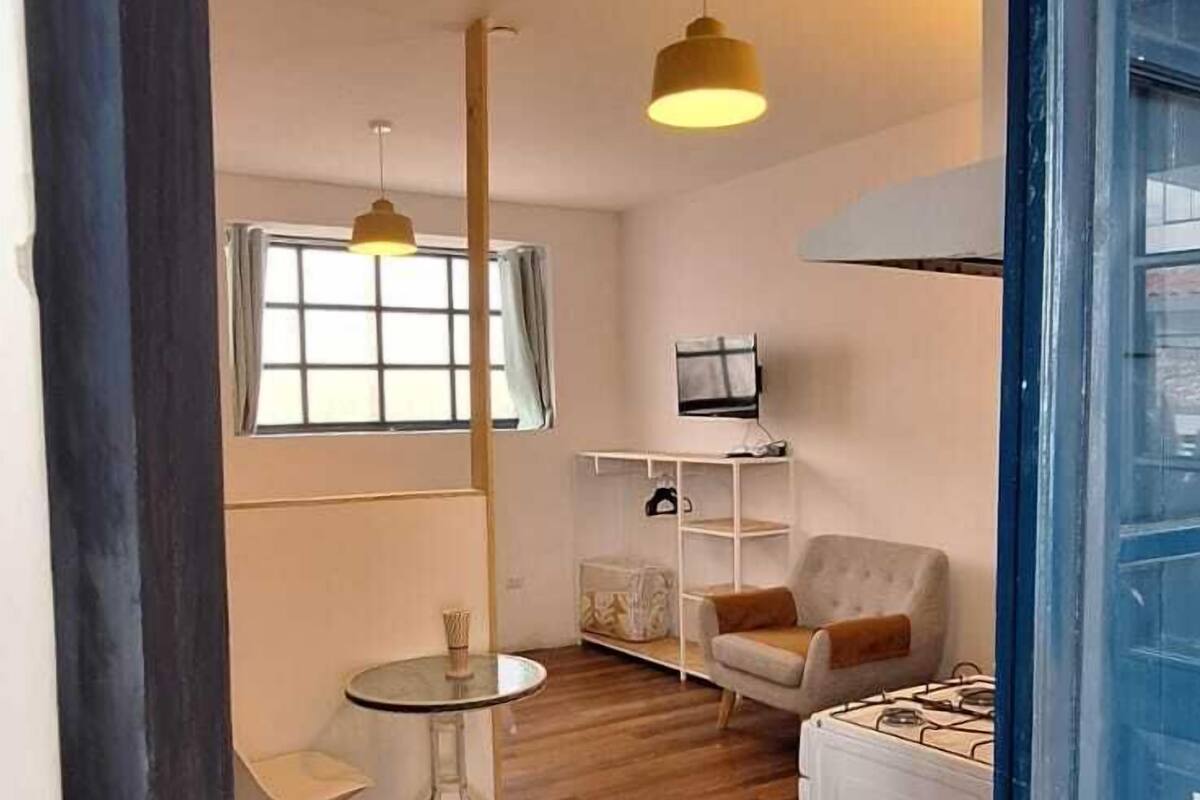 A spacious room with wooden flooring, a round table with chairs, a sofa, and a radiator.