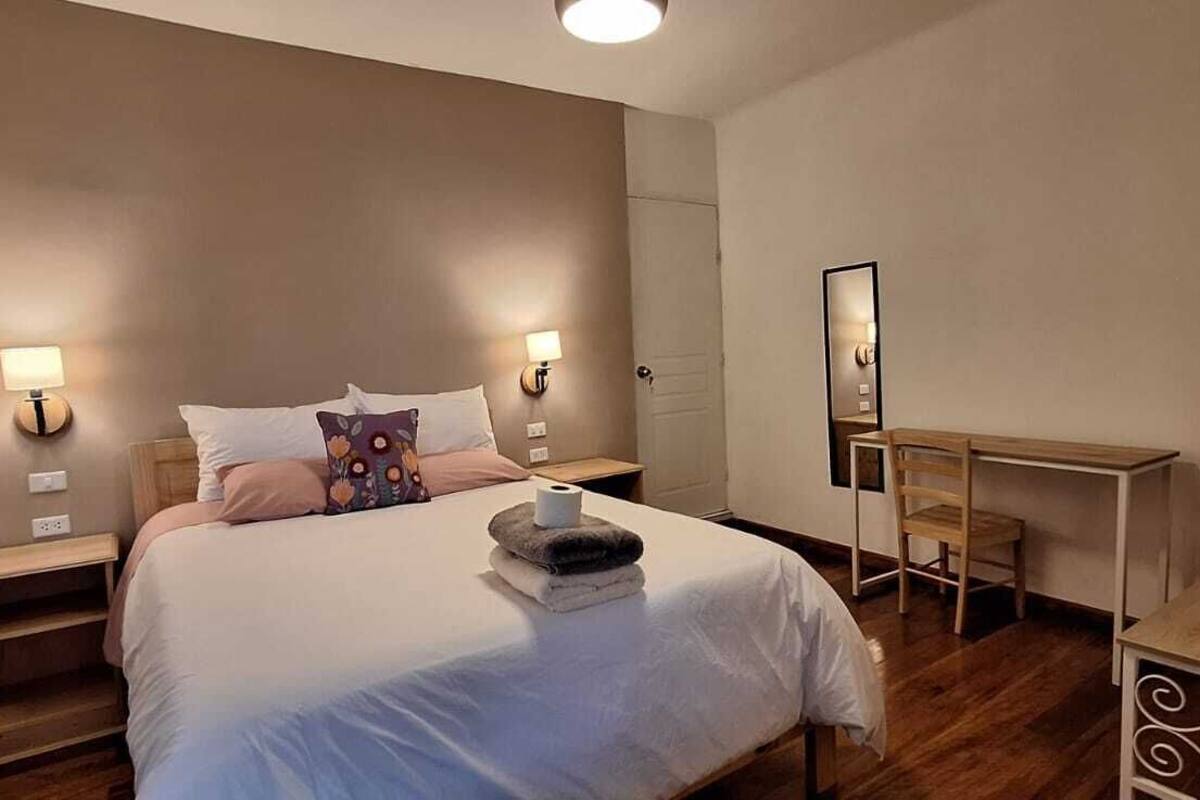 A bedroom with a bed, bedside tables, a desk, and a mirror.