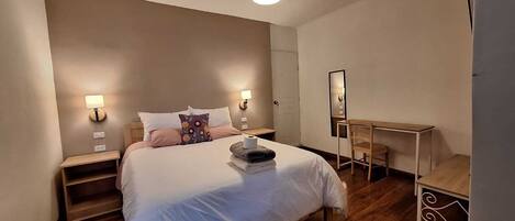 A bedroom with a bed, bedside tables, a desk, and a mirror.