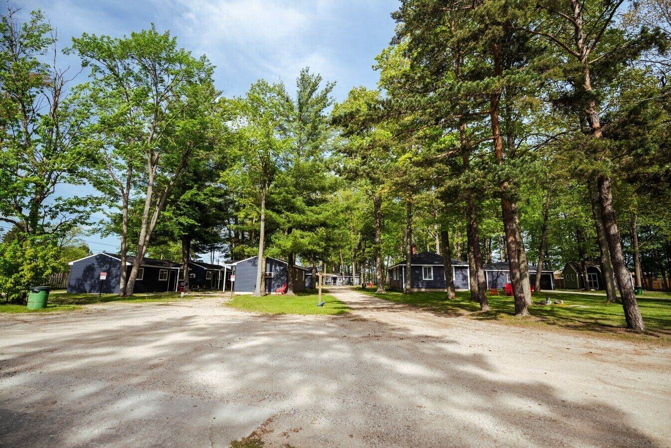 A campground with several cabins, a gravel driveway, and surrounding trees.