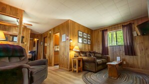 Interior acogedor de una cabaña con sofá, una mesita, lámpara y ventana con cortinas.