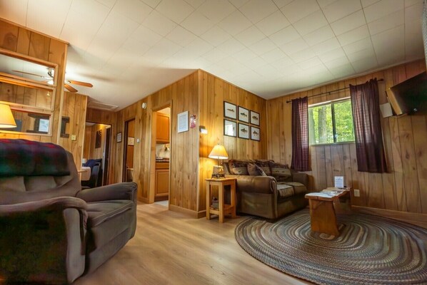 L’intérieur d’un chalet accueillant, avec un canapé, une petite table, une lampe et une fenêtre avec des rideaux.