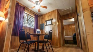 Un interior de madera con una mesa de comedor, sillas, un ventilador de techo y una cama en la habitación contigua.