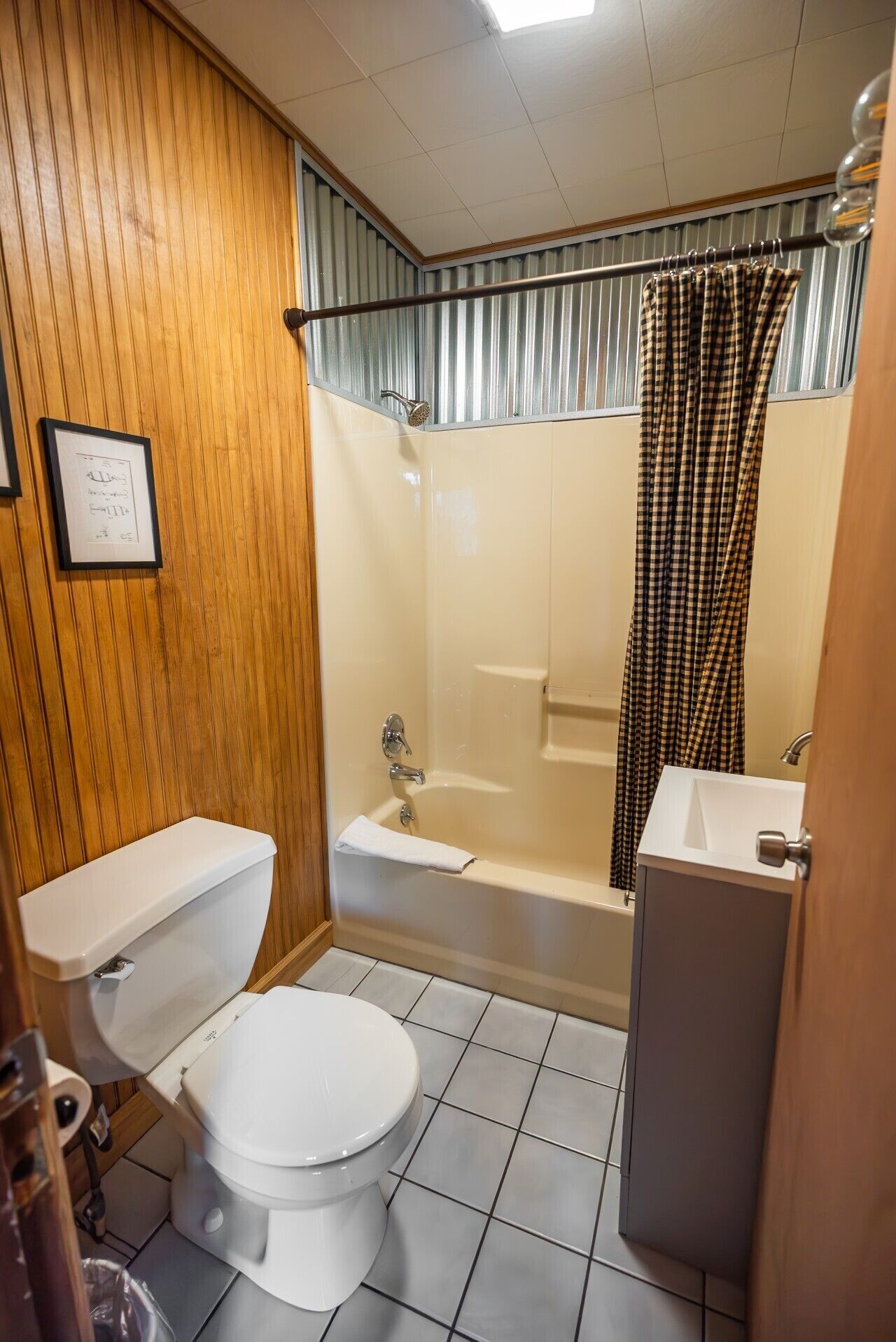 Ein Badezimmer mit Toilette, Waschbecken, Dusche und einer Holzwand.