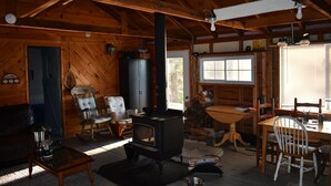 Un intérieur de chalet chaleureux avec un poêle à bois, une table à manger, des chaises et un coin salon comprenant un canapé et une table basse.