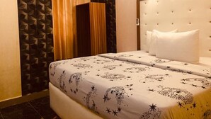 A hotel room with a bed, a headboard, a window with curtains, and an air conditioning unit. - BeamGate Hotel (Uyo)