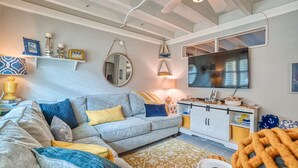 A modern living room with a grey sofa, yellow and blue cushions, a patterned rug, a television, and a decorative mirror.