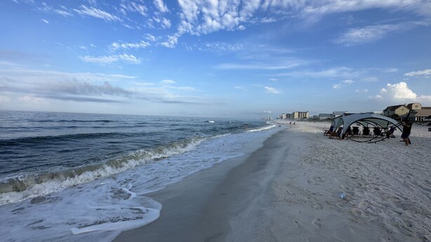 A beach with a clear sky, waves, and a few beach umbrellas.