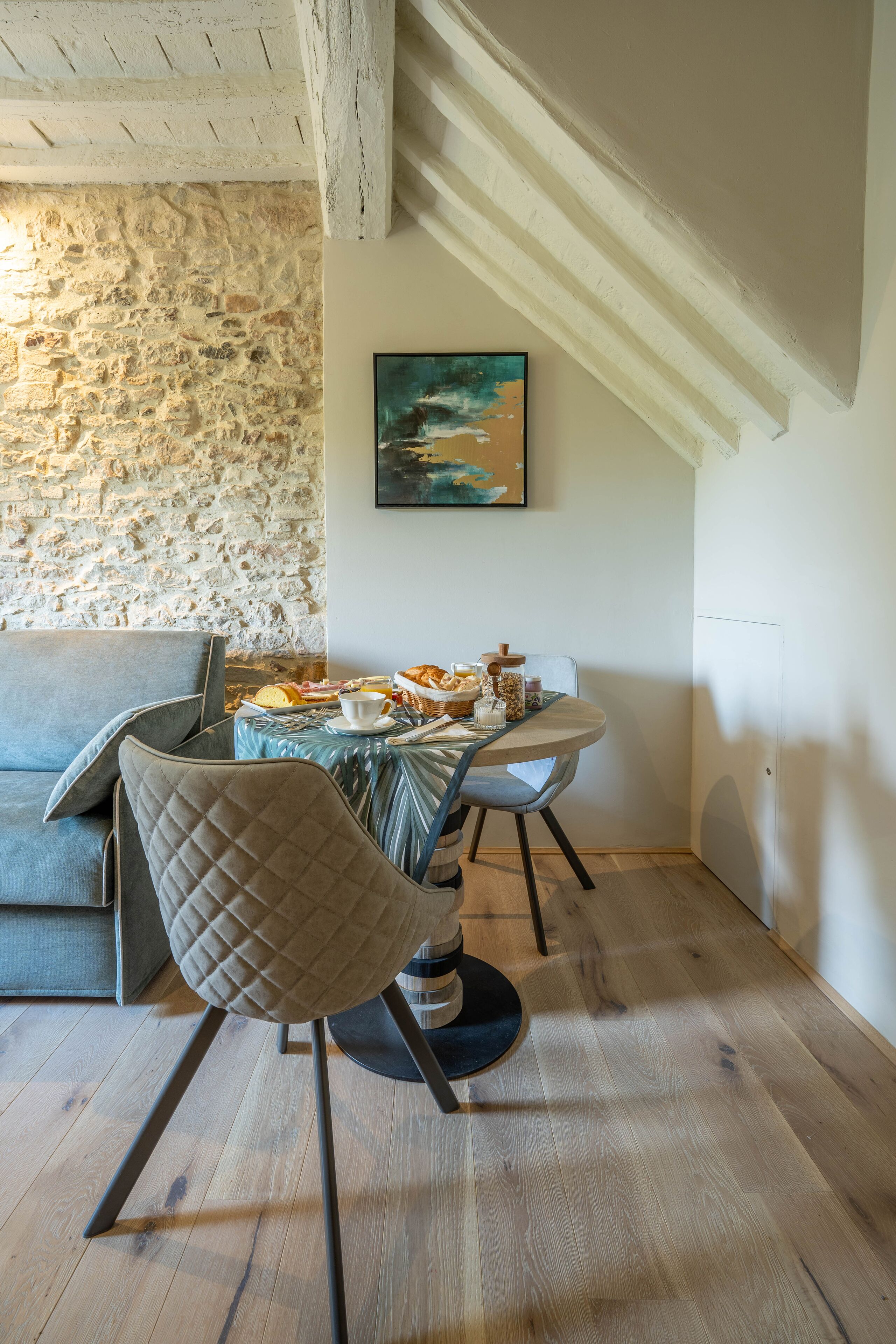 Un comedor con pared de piedra, un cuadro y una mesa servida con comida y bebidas.
