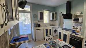 Cocina compacta con lavadora, microondas y un pequeño comedor con mesa.