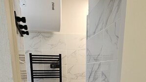 Un baño con toallero negro, alfombra de baño azul y azulejos de mármol blanco.