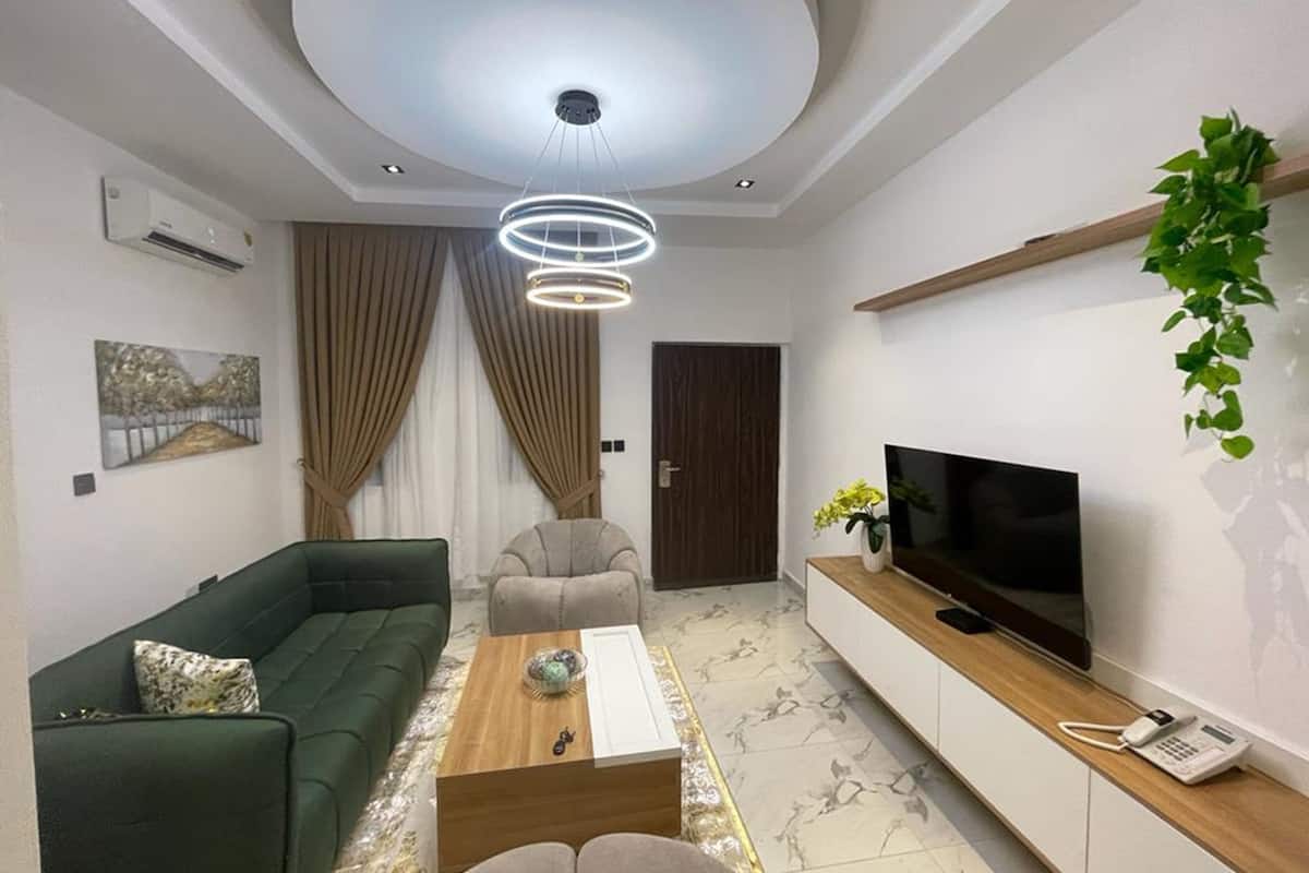 Una sala de estar moderna con un sofá verde, un sillón beige, una mesa de centro, un televisor sobre un mueble de madera y una planta.