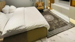 A modern bedroom with a large bed, a TV mounted on the wall, and a seating area with a chair. - All States Apartments (Abuja)