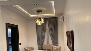 A modern living room with a sofa, a dining table with chairs, and a chandelier. - All States Apartments (Abuja)