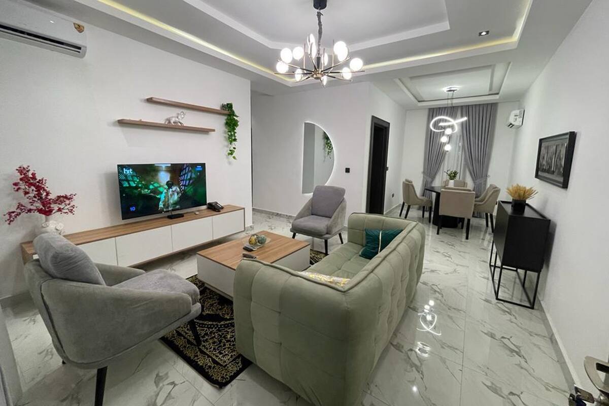 Una sala moderna con un televisor de pantalla plana, un sofá, dos sillones, una mesa de centro y un comedor con mesa y sillas.