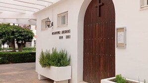 A building with a large wooden door, a white wall with a sign, and potted plants. - Salomar Golf+parking+piscina+tenis (Salobreña)