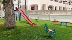 A playground with a red slide, swings, and a seesaw. - Salomar Golf+parking+piscina+tenis (Salobreña)