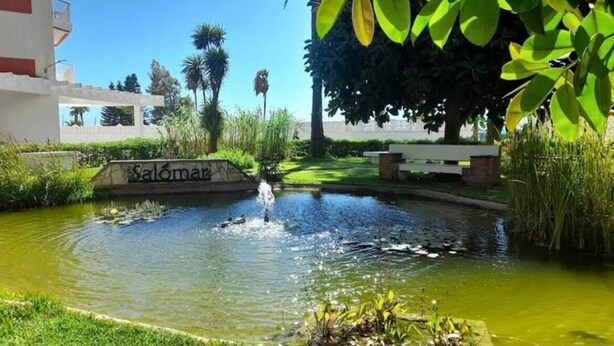 A small pond with a fountain in the center, surrounded by greenery and a sign that reads "Salomán". - Salomar Golf+parking+piscina+tenis (Salobreña)