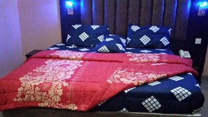 A bed with a headboard, a red and white patterned bedspread, and blue pillows with a geometric design.
