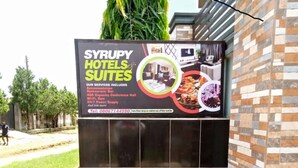 A sign for Syrupy Hotels & Suites advertising services like accommodation, Wi-Fi, 24/7 pantry supply, and a conference hall.
