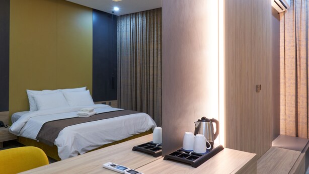 A hotel room with a bed, bedside table, a desk with a chair, and a coffee maker. - Arcade Sinclair (Abuja)