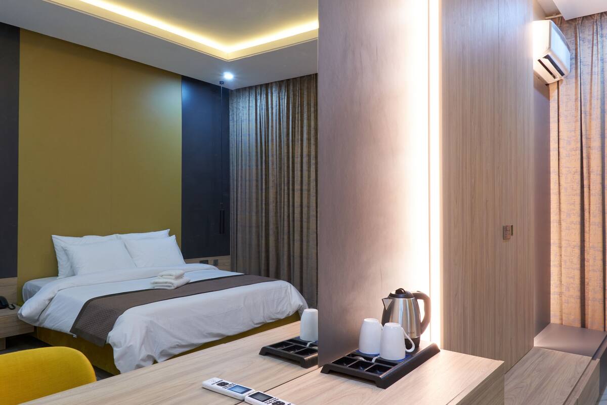 A hotel room with a bed, bedside table, a desk with a chair, and a coffee maker.
