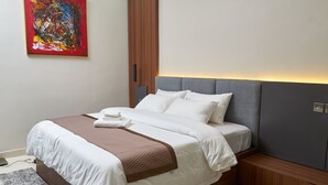 A neatly made bed with white and brown linens, a gray headboard, and a wooden nightstand. - Arcade Sinclair (Abuja)