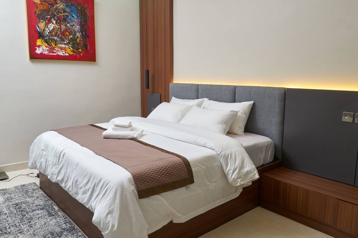 A neatly made bed with white and brown linens, a gray headboard, and a wooden nightstand.