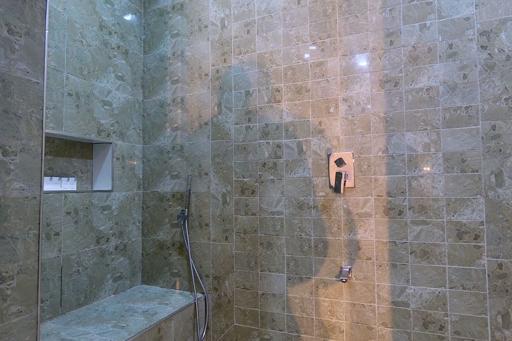 A shower area with a tiled wall, a handheld showerhead, and a wall-mounted control panel.