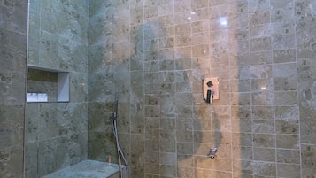 A shower area with a tiled wall, a handheld showerhead, and a wall-mounted control panel.